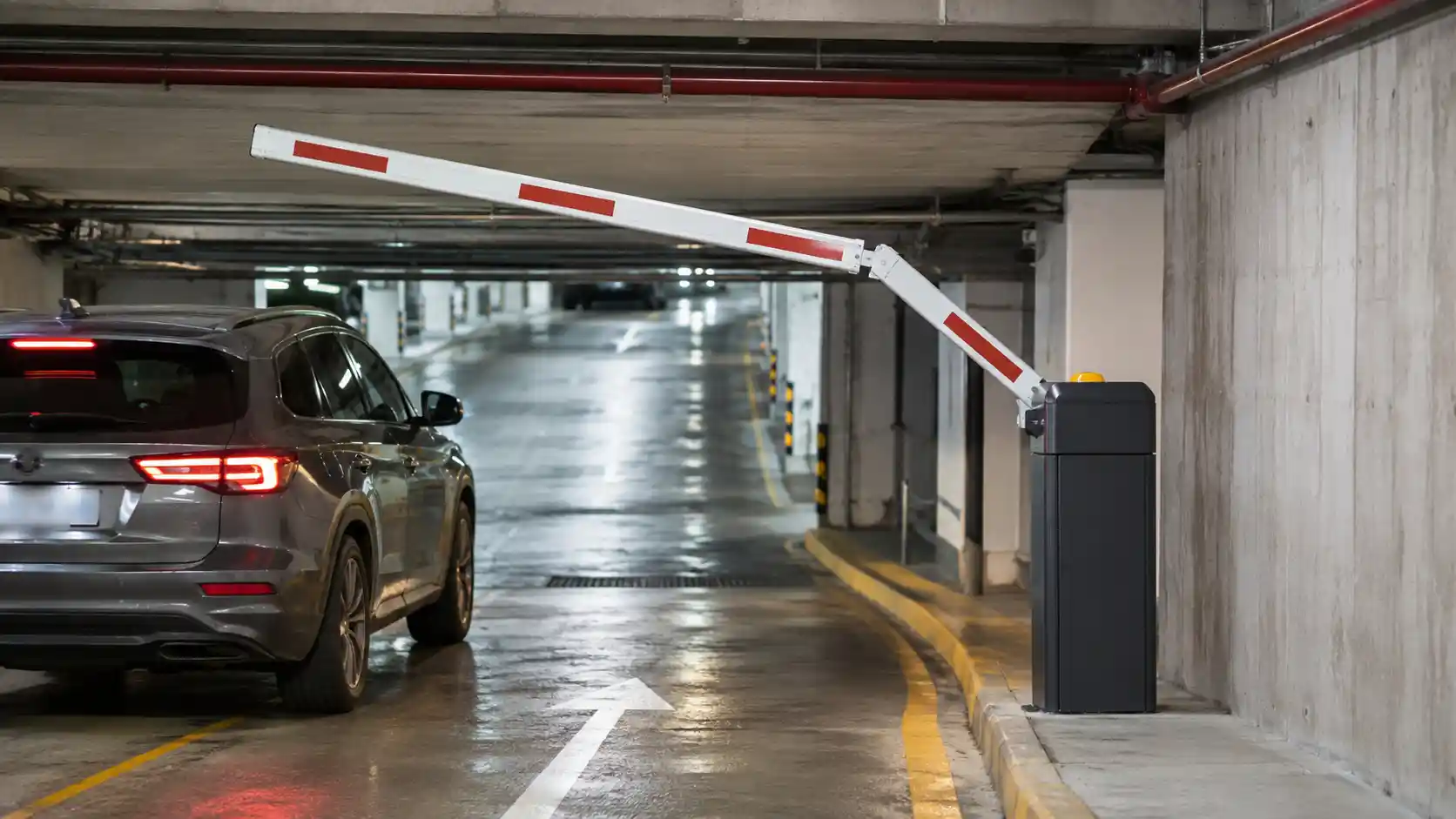 Folding boom arm barrier gate used in an underground parking garage with limited ceiling clearance and vehicle access contr